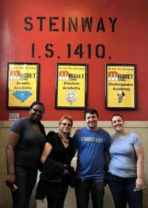 four people smiling and standing in front of a red wall in a school