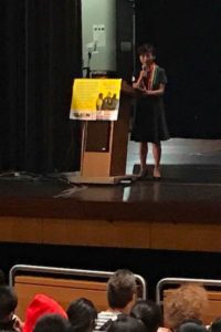 woman in black on stage in a school auditorium