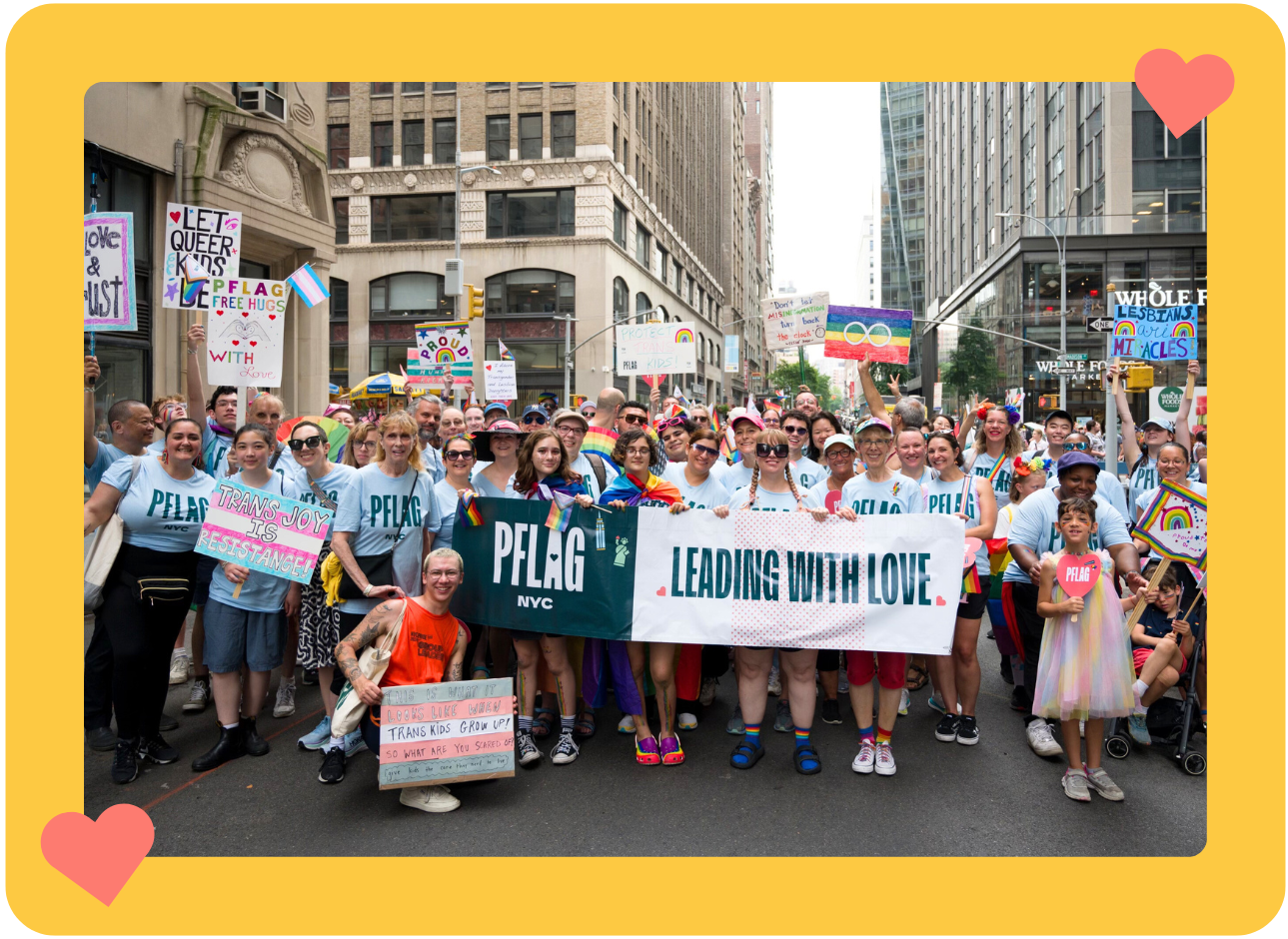 A photo of a large group of diverse people of different ages holding up banners and signs and wearing PFLAG NYC shirts at the 2024 NYC Pride March