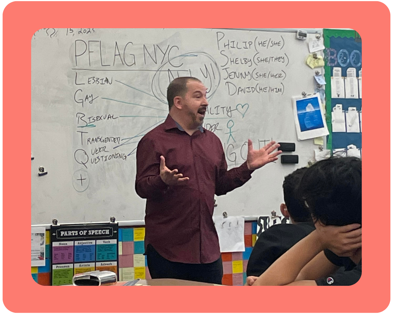 A coral-framed photo of a PFLAG Safe Schools volunteer speaking and gesturing at the front of a room full of students in a classroom