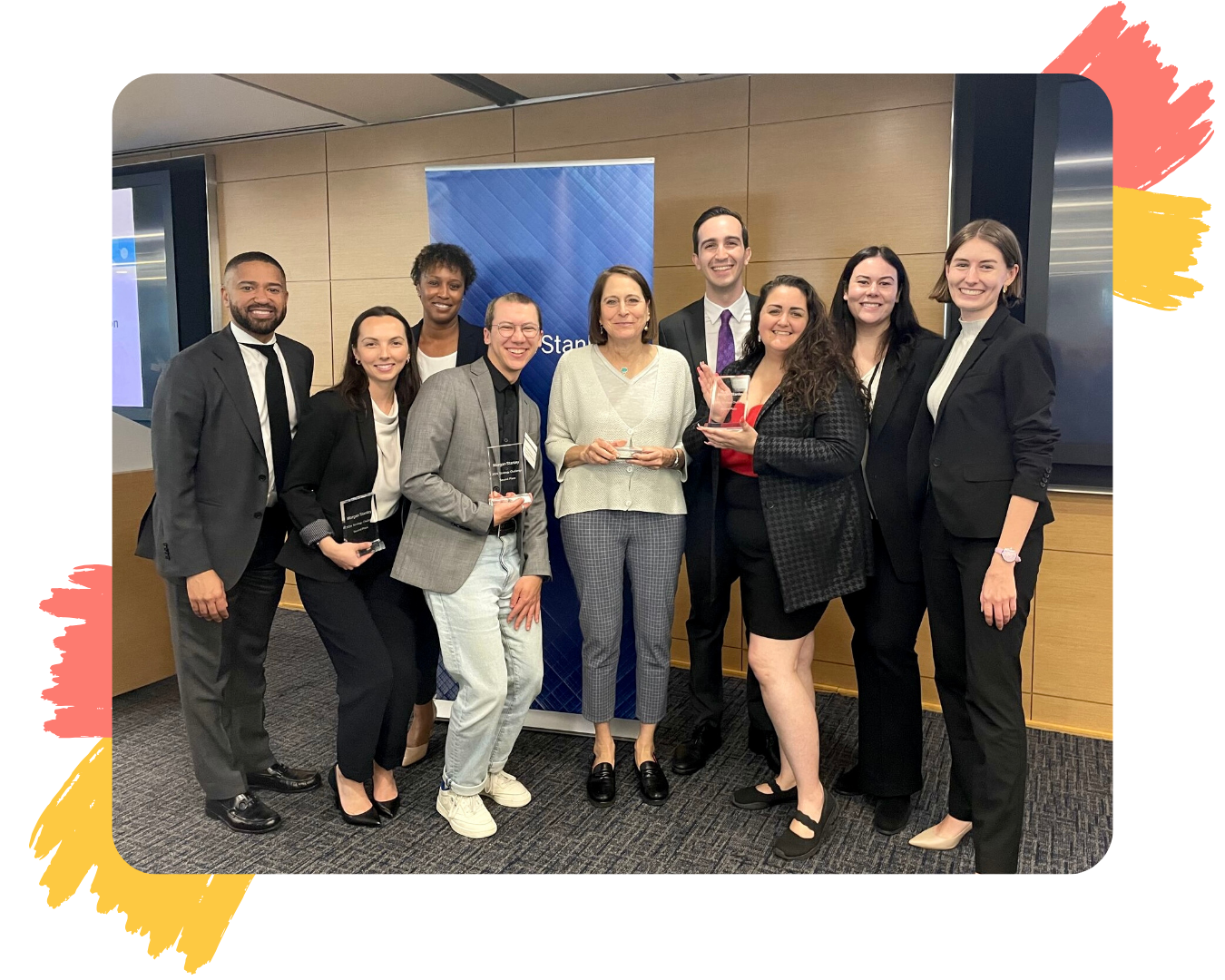 A group of nine diverse people standing together, including PFLAG NYC's Executive Director, Melissa, and Director of Education Programs, Clark, holding up clear glass plaques.